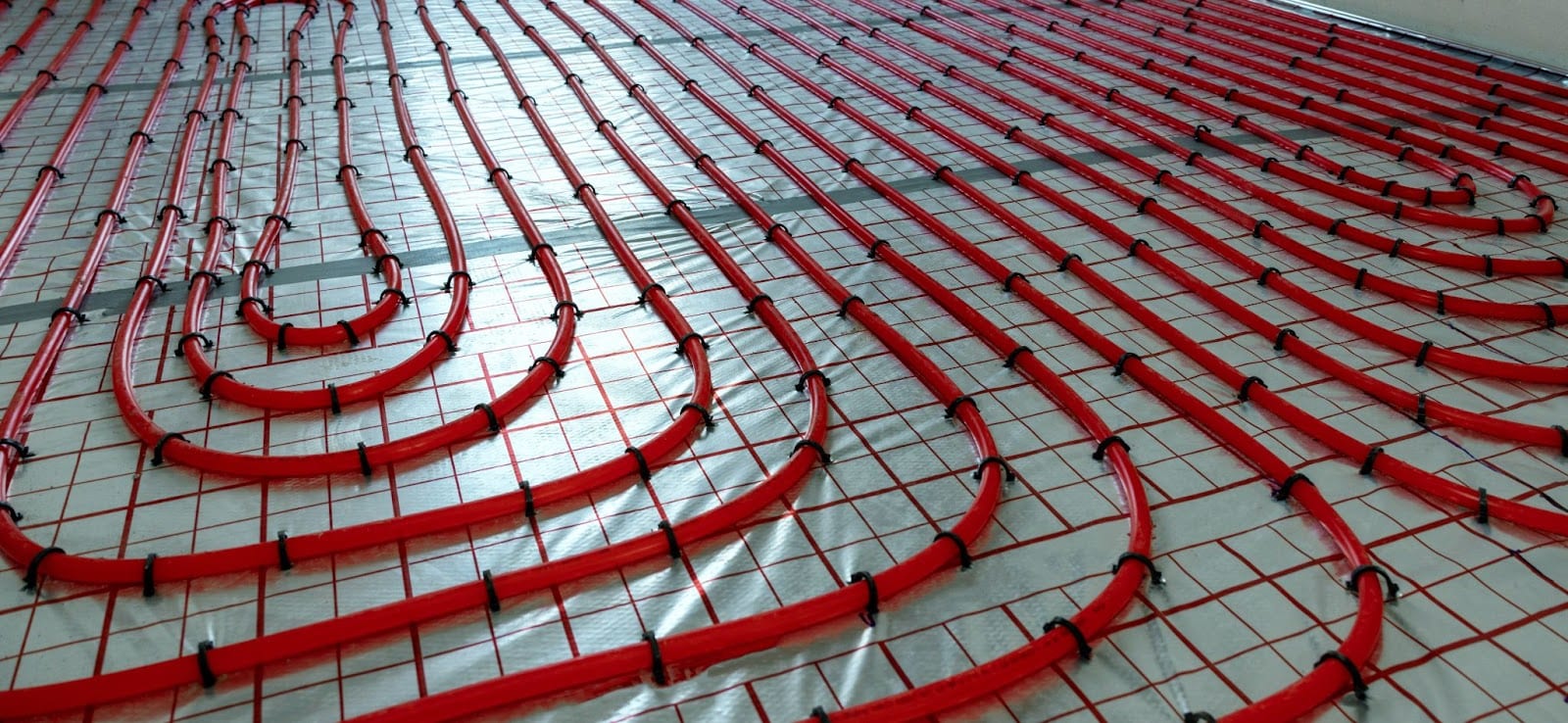A spacious room featuring red heating pipes, indicative of a radiant floor heating system.