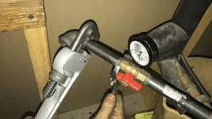 A person holding a wrench and a pipe in a room during a gas line installation.