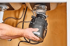 A man fixing a sink drain under a cabinet with a garbage disposal unit.