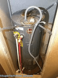 Old water heater in cramped space with hose, needs replacing