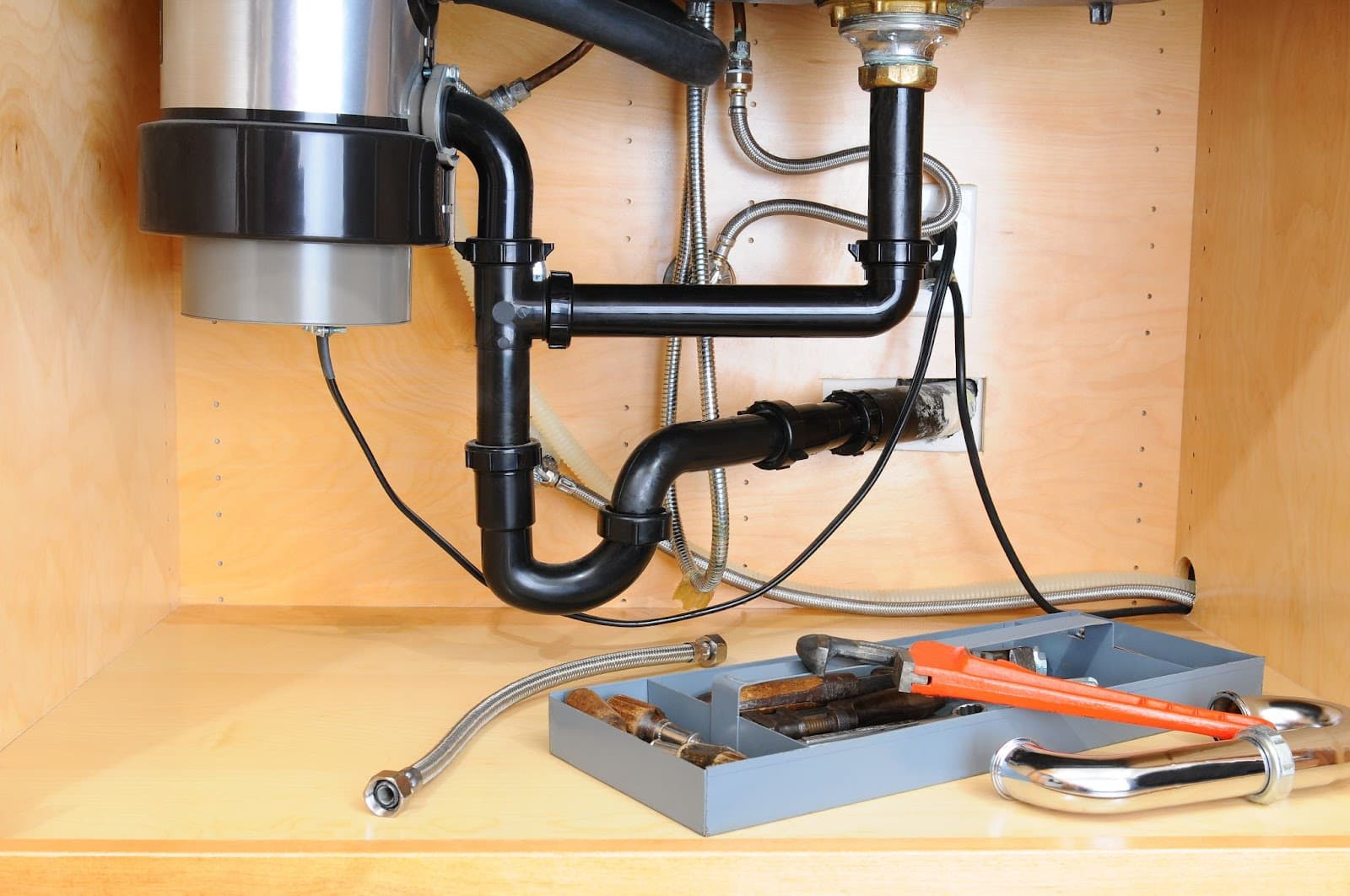 Sink under cabinet with garbage disposal unit, indicating professional plumber for repairs.