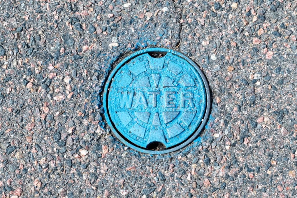 A blue manhole cover labeled Water indicating a broken water main, highlighting the need for professional plumbing services.