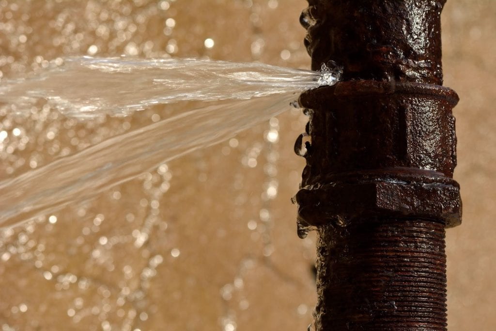 Close-up of burst water pipe with water gushing out, causing water damage.