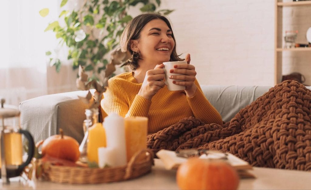 A woman relaxes on a couch with coffee and a pumpkin, embodying a warm fall atmosphere