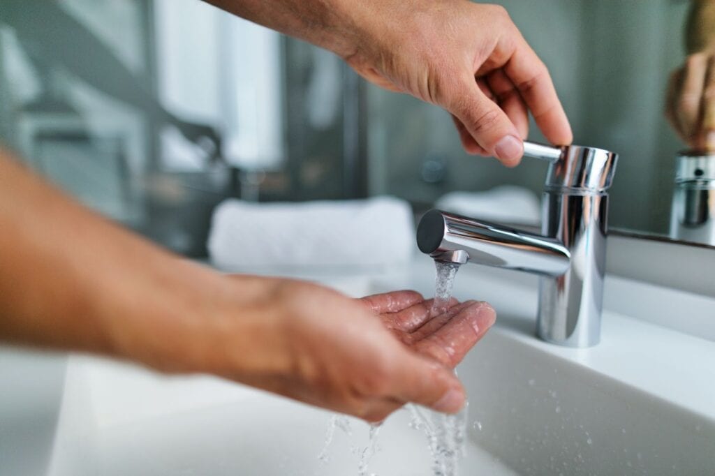 A person washing their hands under a modern bathroom faucet with water flowing.