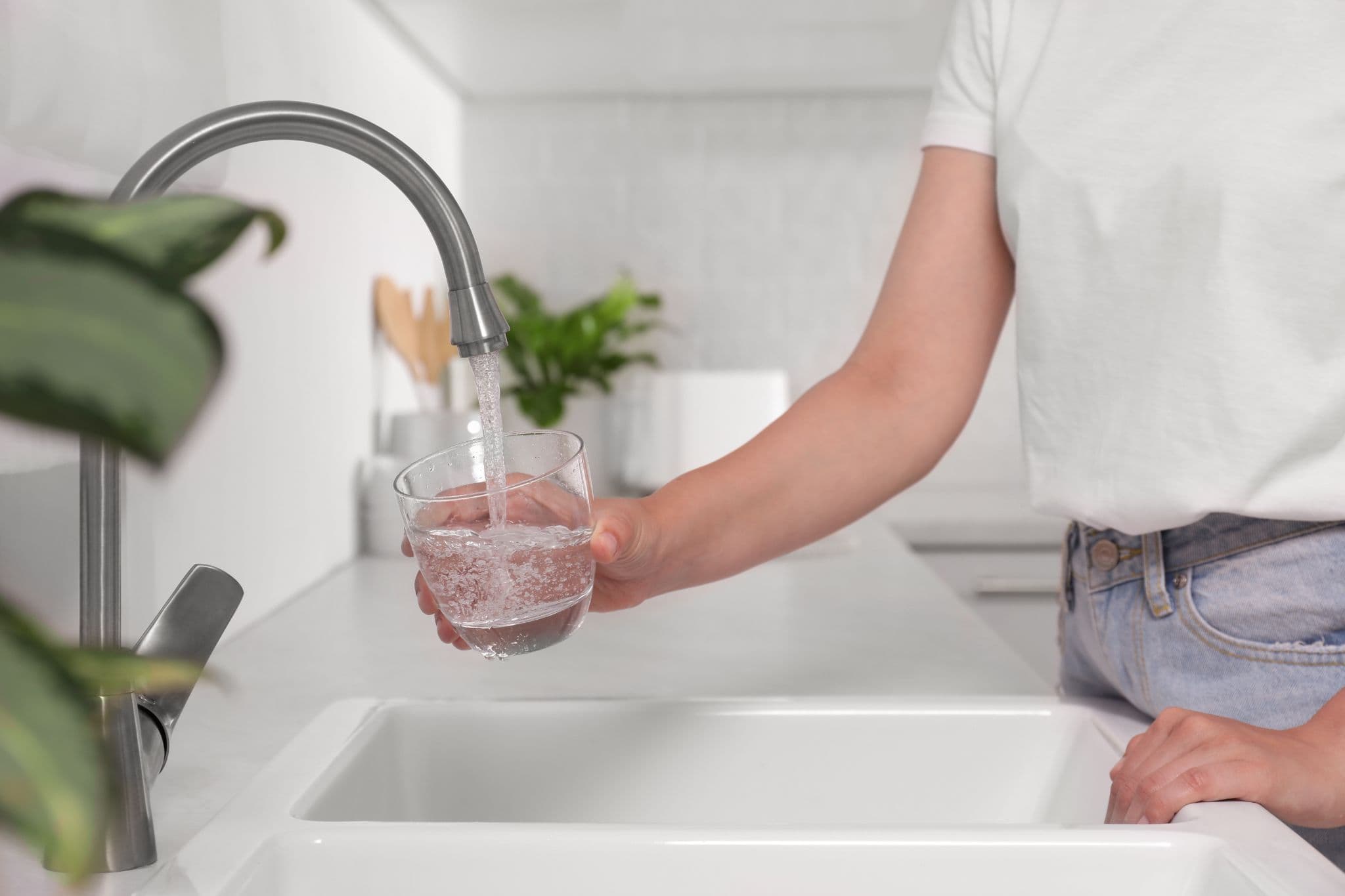 A person filling a clear glass with water from a kitchen faucet.