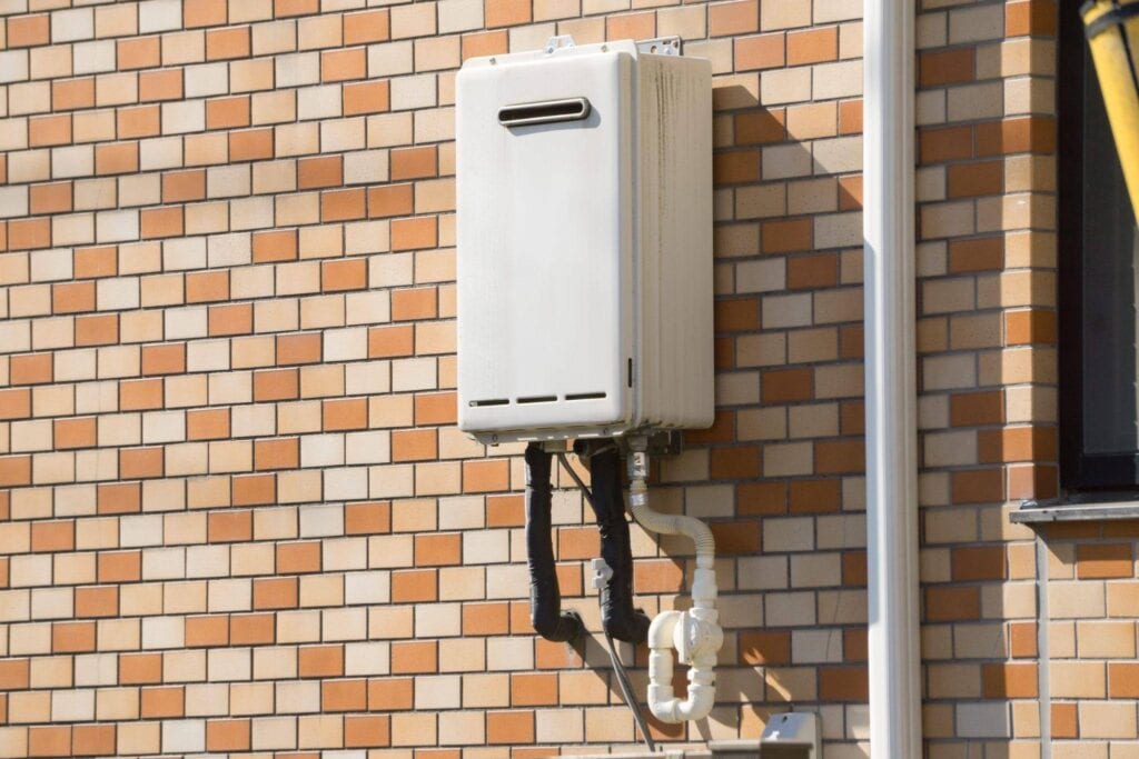 A white water heater installed on a textured brick wall