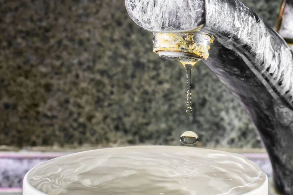A faucet is pouring clear water into a white bowl creating ripples on the surface