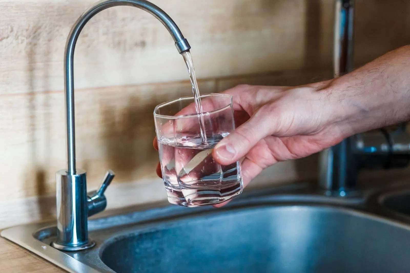 A person holds a glass of water taken from a kitchen sin showcasing a moment of hydration in a home setting