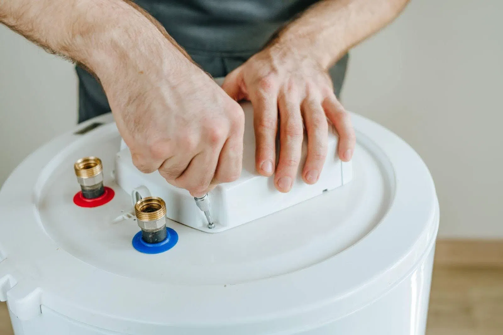 A man repairs a water heater focused on the task with tools in hand and parts scattered around him