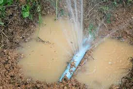 Water pipe releasing water into the soil, forming a wet patch.