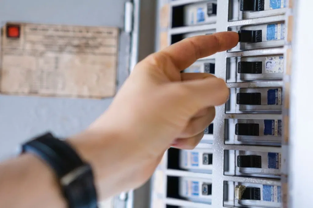 Hand flipping a switch in an electrical panel.