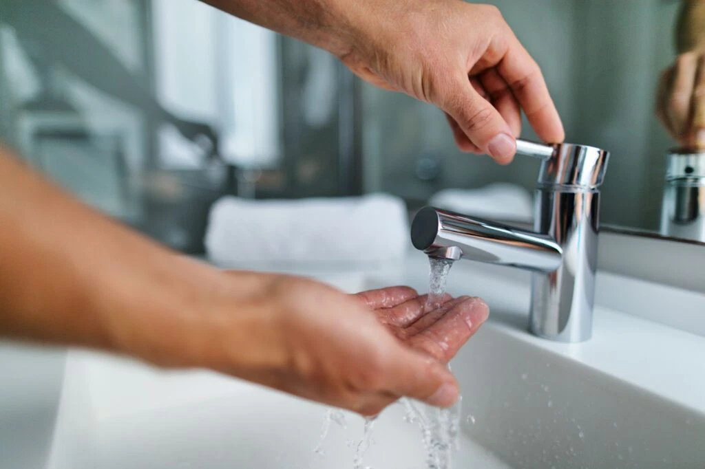 A person washing their hands under a modern bathroom faucet with water flowing.