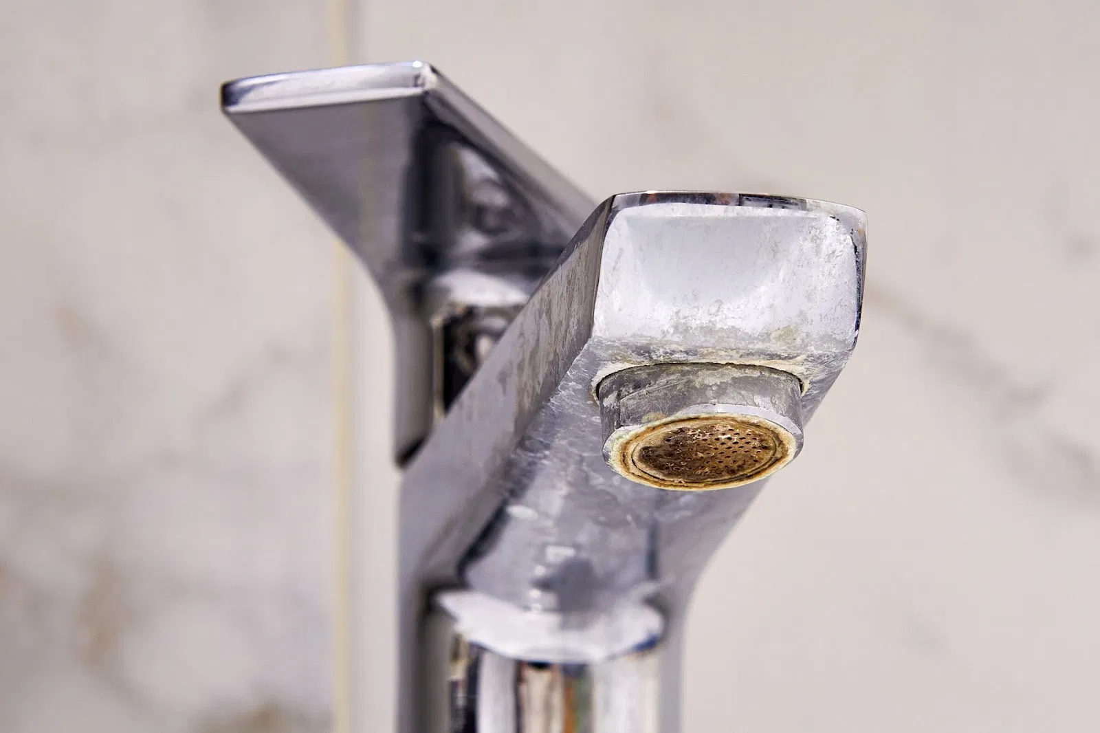 A close-up view of a chrome bathroom faucet heavily covered in white limescale and mineral buildup.