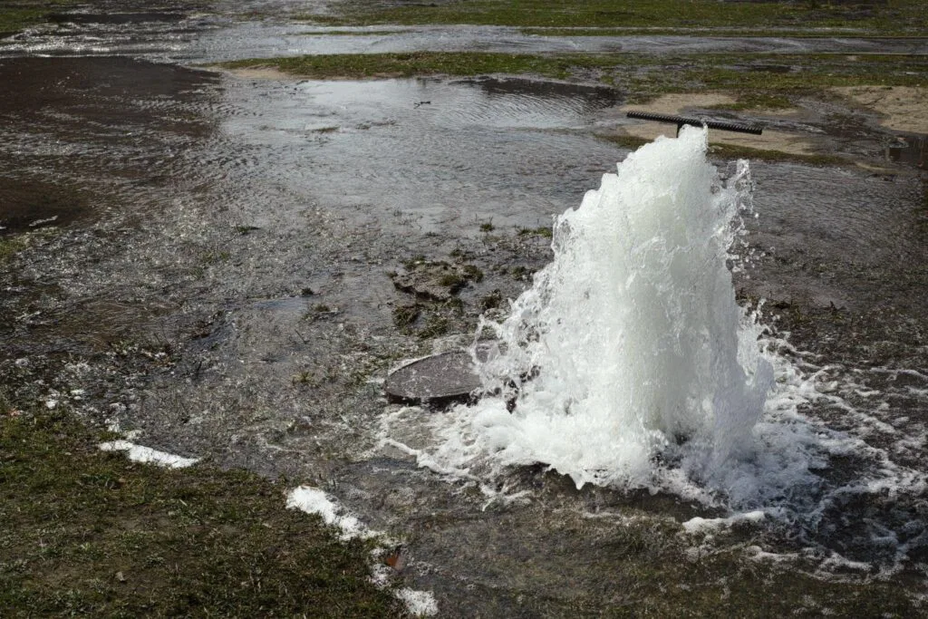 Water shoots high into the air from an open fire hydrant on a city street