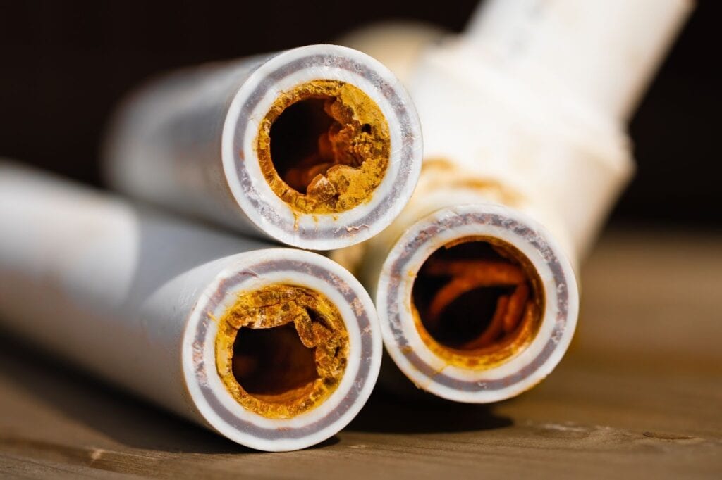 This image shows cross-sections of old galvanized steel water pipes that have been cut open, revealing severe internal corrosion and rust buildup.
