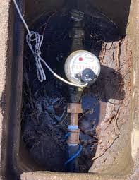 Water meter in concrete box with attached hose, connected to water main