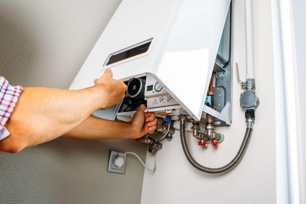 A man repairs a gas boiler in a well-lit room focused on the task at hand Tools are scattered nearby